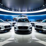 A sleek, futuristic showroom displays five high-performance electric vehicles, each exuding luxury and cutting-edge technology. Bright lights illuminate the sleek curves and polished surfaces, creating an atmosphere of innovation and sophistication